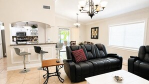 A modern living room with a black leather sofa, a white coffee table, and a dining area with bar stools. - House 3B2B (Tampa)