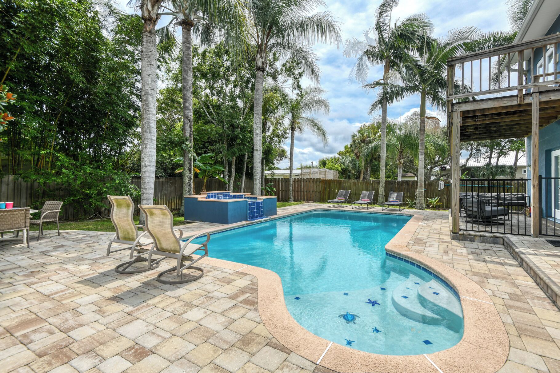 A swimming pool with a curved edge, surrounded by a patio area with chairs and a wooden deck.