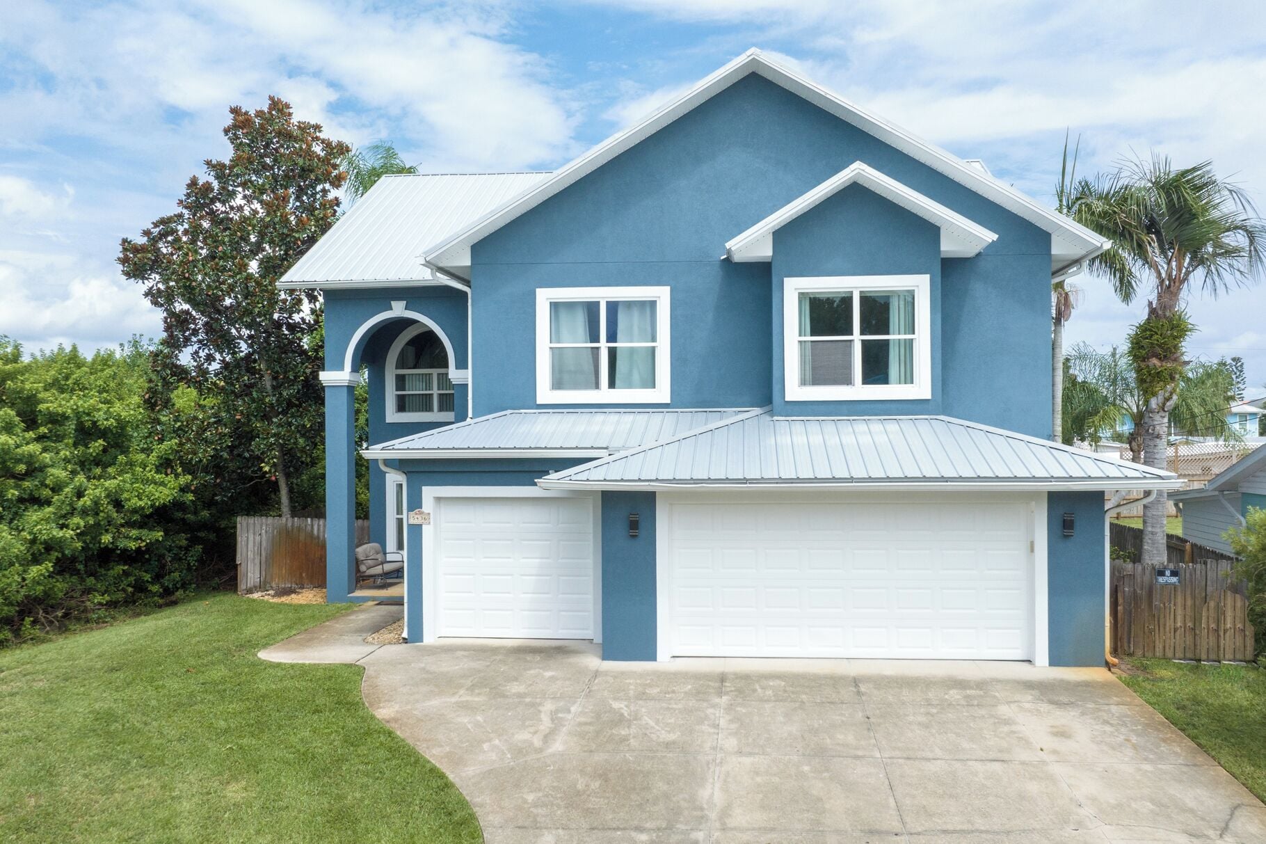 A two-story house with a blue exterior and white trim, featuring two garage doors and a front entrance.