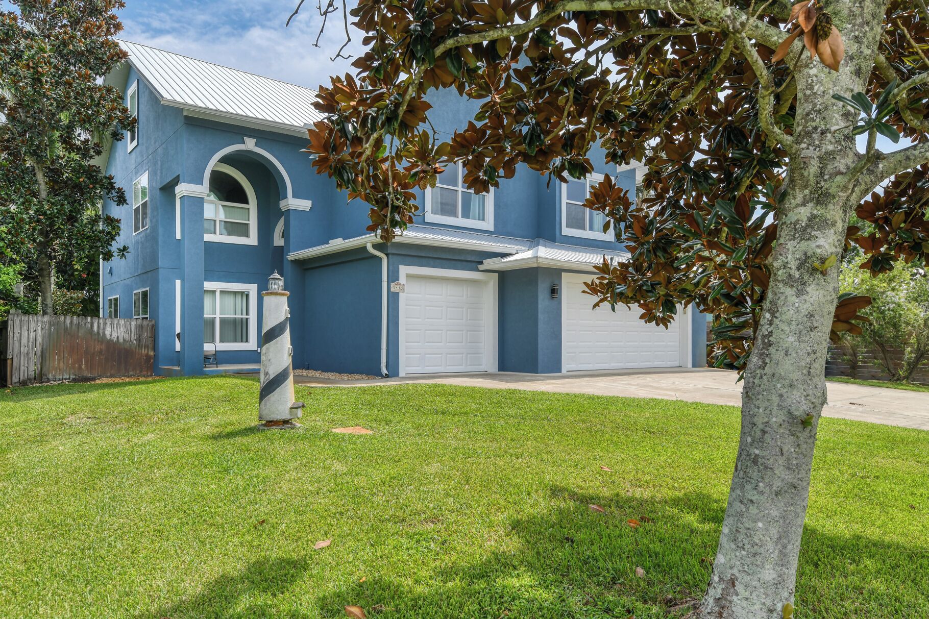 A two-story house with a blue exterior, white garage doors, and a well-maintained lawn.