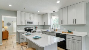 Una cocina moderna con armarios blancos, una isla central con taburetes, microondas, estufa y lavavajillas.