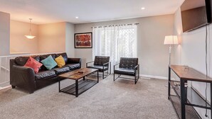 Una sala de estar con sofá, dos sillones, una mesa de centro, televisor y lámpara.