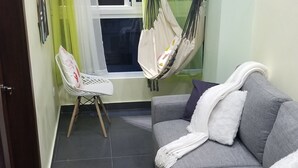 Ein Wohnzimmer mit grauem Sofa, weißem Sessel, einer Hängematte und einem karierten Teppich.