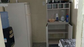 Une cuisine compacte équipée d’un réfrigérateur, d’une cuisinière et d’une étagère contenant divers ustensiles de cuisine.