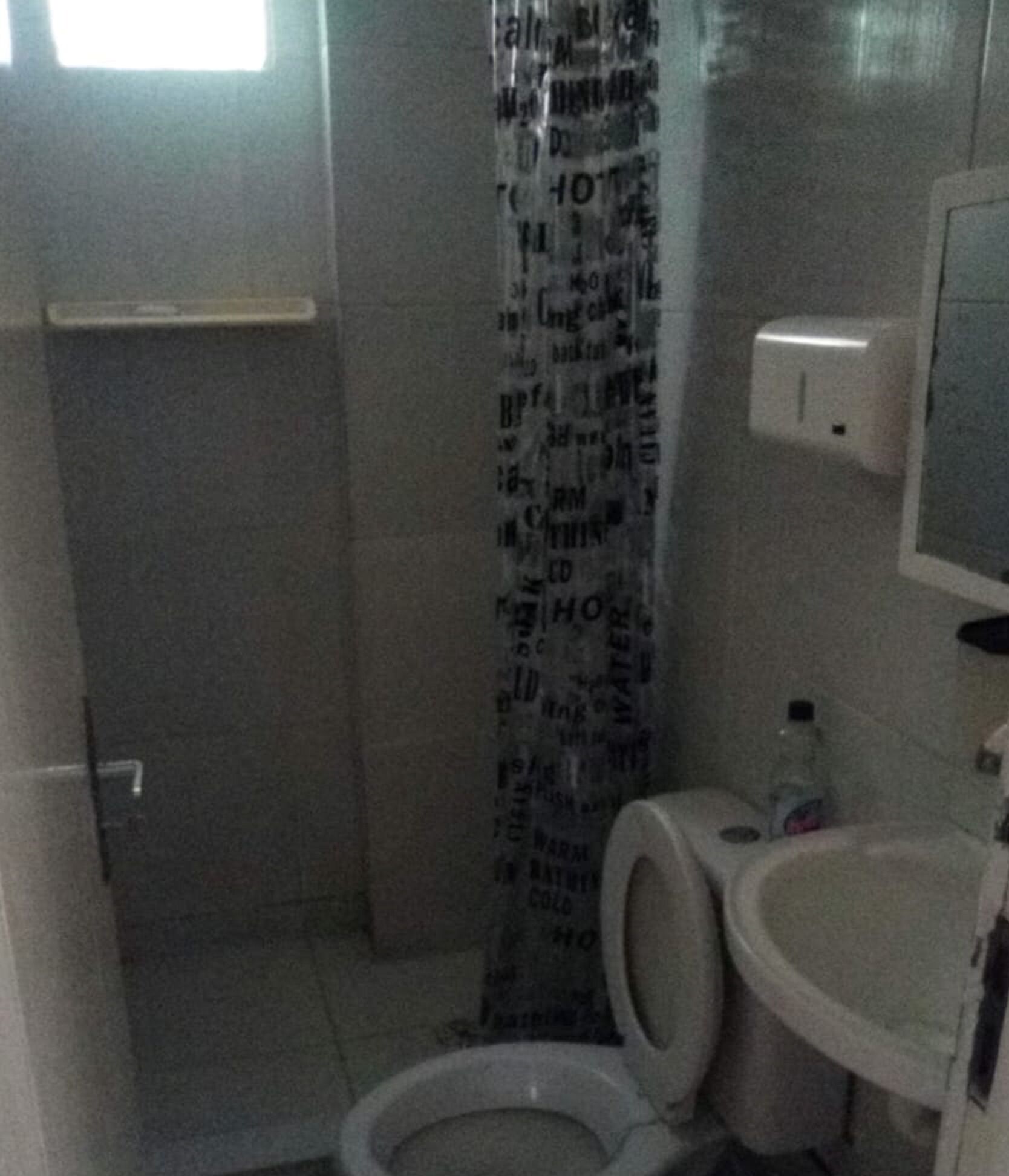 Ein kleines, schlichtes Badezimmer mit Toilette, Waschbecken und Duschvorhang.
