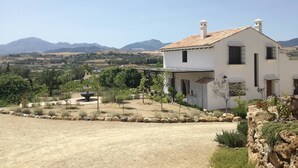A white building with a tiled roof, surrounded by a landscaped garden with a fountain, set against a mountainous backdrop. - 3-Bed Andalusian House with Private Pool & Garden! (Pizarra)