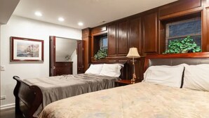 Une chambre d’hôtel avec deux lits, un lambris en bois, une grande fenêtre avec des stores, une table de chevet avec une lampe et un tableau encadré au mur.