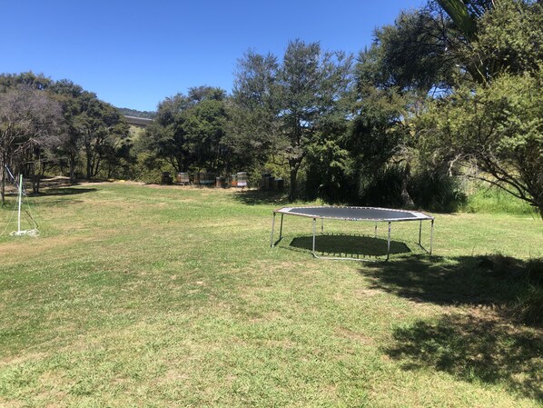 A trampoline in a grassy outdoor area with trees and a clear sky.