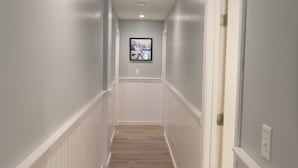 A hallway with white wainscoting, a wooden floor, and recessed ceiling lights.
