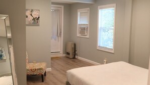 A bedroom with a bed, a chair, a dresser, and a window with blinds.