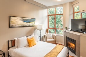 Relax in a stylish room with a large bed, flat-screen TV, and fireplace, surrounded by lush greenery views.