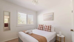 A bedroom with a bed, a bedside table, a window with blinds, a mirror, and a painting on the wall. - Salty Dayz Retreat—Steps from Busselton Beach (Broadwater)