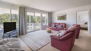 Una sala de estar moderna con un televisor de pantalla plana, un conjunto de sofá y un amplio ventanal con vistas al exterior.
