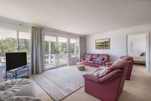 Una sala de estar moderna con un televisor de pantalla plana, un conjunto de sofá y un amplio ventanal con vistas al exterior.