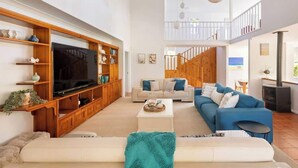 A spacious living room with a large TV, wooden entertainment unit, and a blue sofa. - Salty Dayz Retreat—Steps from Busselton Beach (Broadwater)