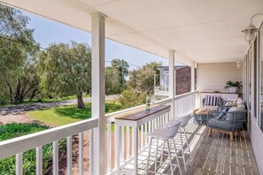 A covered outdoor area with a wooden deck, white railings, and seating furniture.
