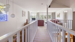 A spacious corridor with a white railing, a staircase, and a view of a balcony area with seating. - Salty Dayz Retreat—Steps from Busselton Beach (Broadwater)