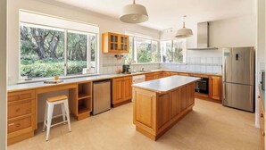 A modern kitchen with wooden cabinets, a large island, and a view of greenery outside. - Salty Dayz Retreat—Steps from Busselton Beach (Broadwater)