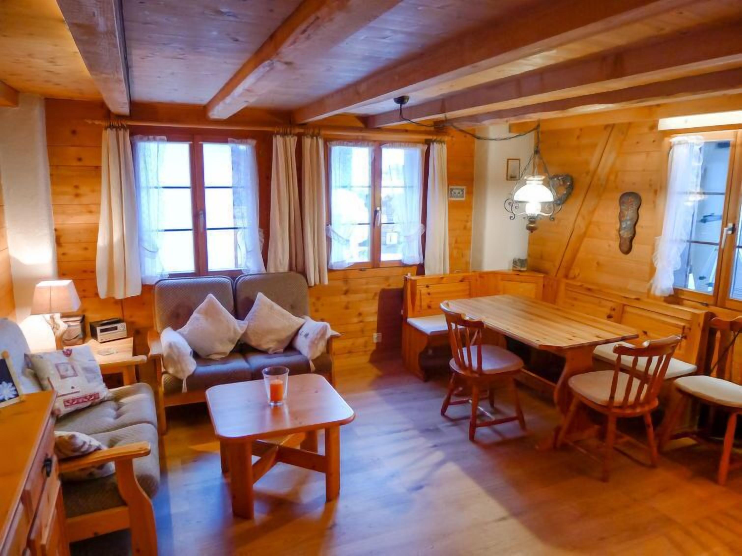 A cozy cabin interior with a wooden dining table, chairs, a sofa, and a small table with a glass.
