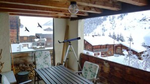 Eine Holzterrasse mit Tisch und Stühlen, einem Teleskop und Blick auf schneebedeckte Häuser in der Ferne.