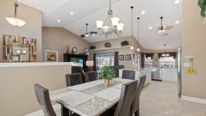 A spacious kitchen with a dining area, featuring granite countertops, a chandelier, and a large island with a sink and stove.