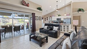A spacious living area with a glass coffee table, leather sofas, and a kitchen in the background.