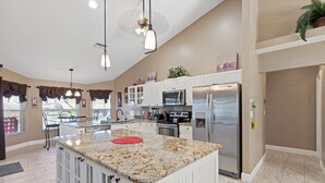 A spacious kitchen with granite countertops, white cabinetry, a stainless steel refrigerator, and a central island.