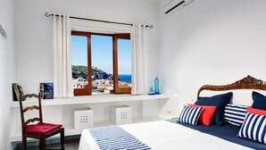 A bedroom with a large bed, a chair, a window with curtains, a shelf with books, and a view of a coastal town. - Nice apartment for 6 guests with WIFI, A/C, TV, terrace and panoramic view (Sorrento)