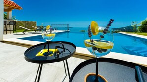 Ein Poolbereich mit zwei Tischen, einer mit einem gelben Handtuch und Sonnenbrille, der andere mit einem Getränk und einer Zitronenscheibe.