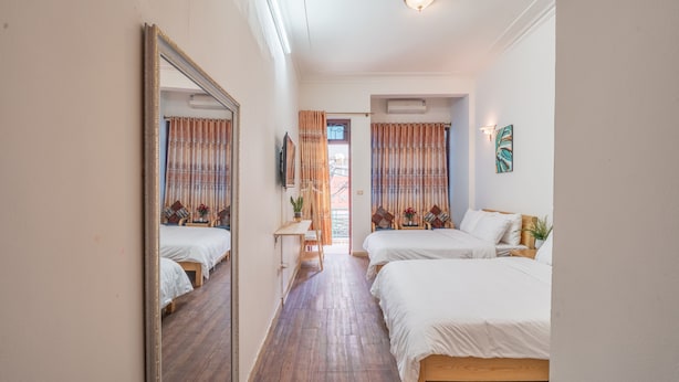 Une chambre d’hôtel avec deux lits, une petite table, un miroir et une porte donnant sur un balcon.