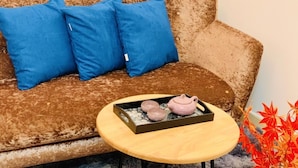 Un canapé marron avec des coussins bleus et une petite table en bois sur laquelle se trouve un plateau contenant une théière et deux tasses.