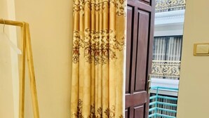 Une pièce avec une étagère en bois, un rideau à motifs floraux et une vue sur un balcon doté d’une balustrade.