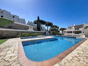 A swimming pool with stone tiles, a stone wall, and a clear blue sky. - JARDINS II 1-9 Roses / Roses - INTERimmo (Rosas / Roses)