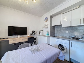 A compact kitchen with a washing machine, a coffee maker, and a flat-screen TV. - JARDINS II 1-9 Roses / Roses - INTERimmo (Rosas / Roses)