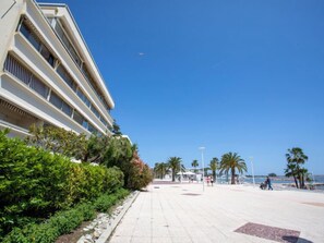 Un hotel sulla spiaggia con una lunga passeggiata lastricata che conduce al mare, palme e cielo azzurro.