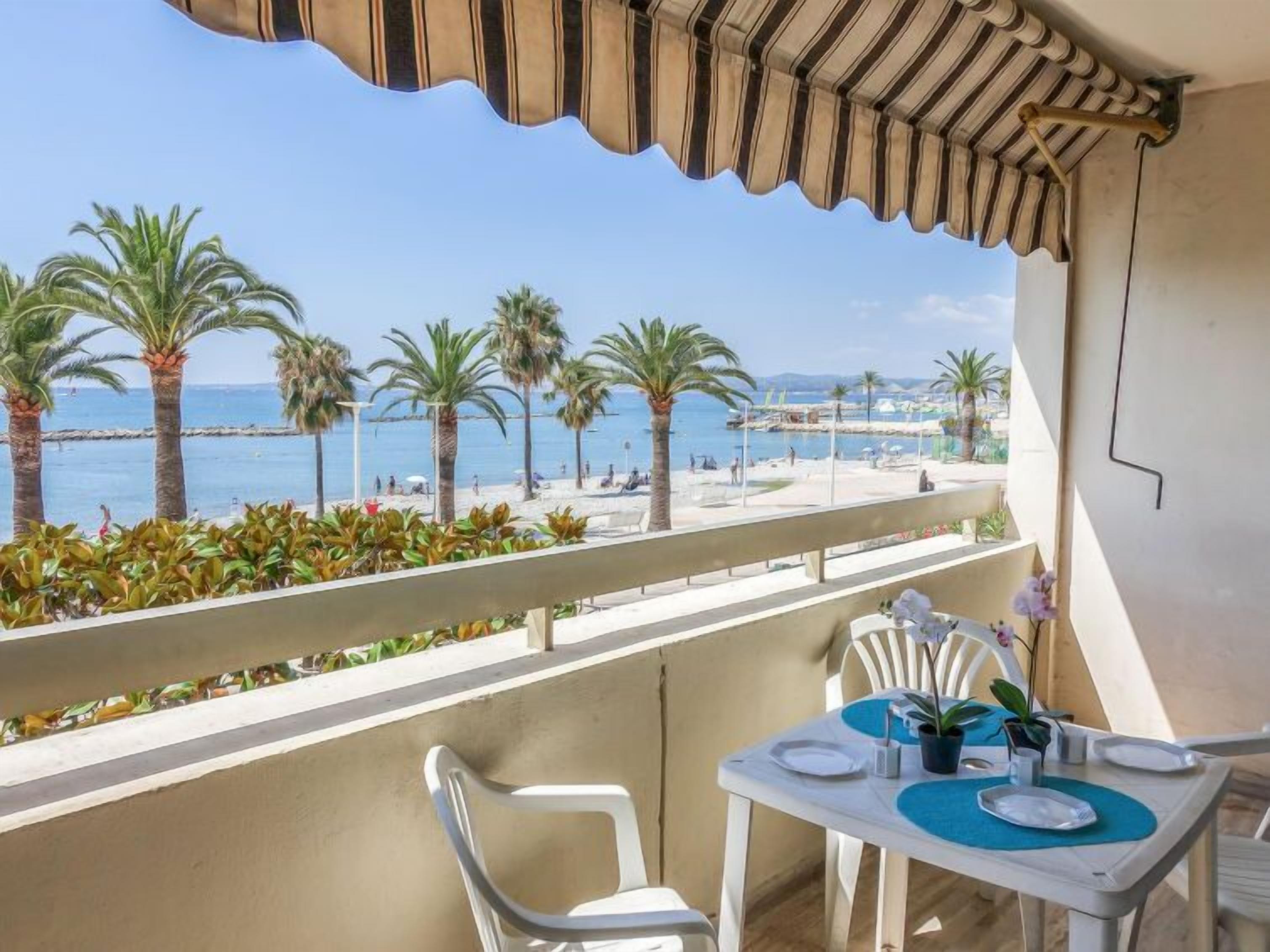 A balcony with a table set for two, overlooking a beach with palm trees and the sea.