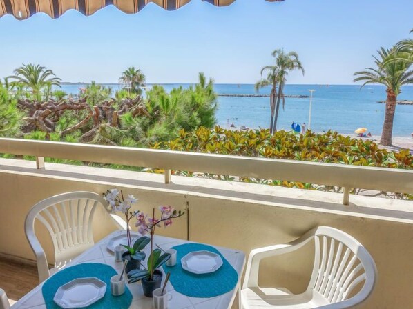 Un balcone con un tavolo apparecchiato per due, vista su una spiaggia con palme e il mare.