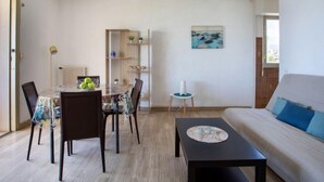 Ein Wohnzimmer mit Esstisch, Stühlen, einer Couch und einem Couchtisch. An der Wand befindet sich ein Bücherregal und ein Gemälde.