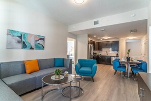 Un salon moderne avec un canapé gris, un fauteuil bleu et un coin repas comprenant des chaises et une table, le tout dans des tons bleus.