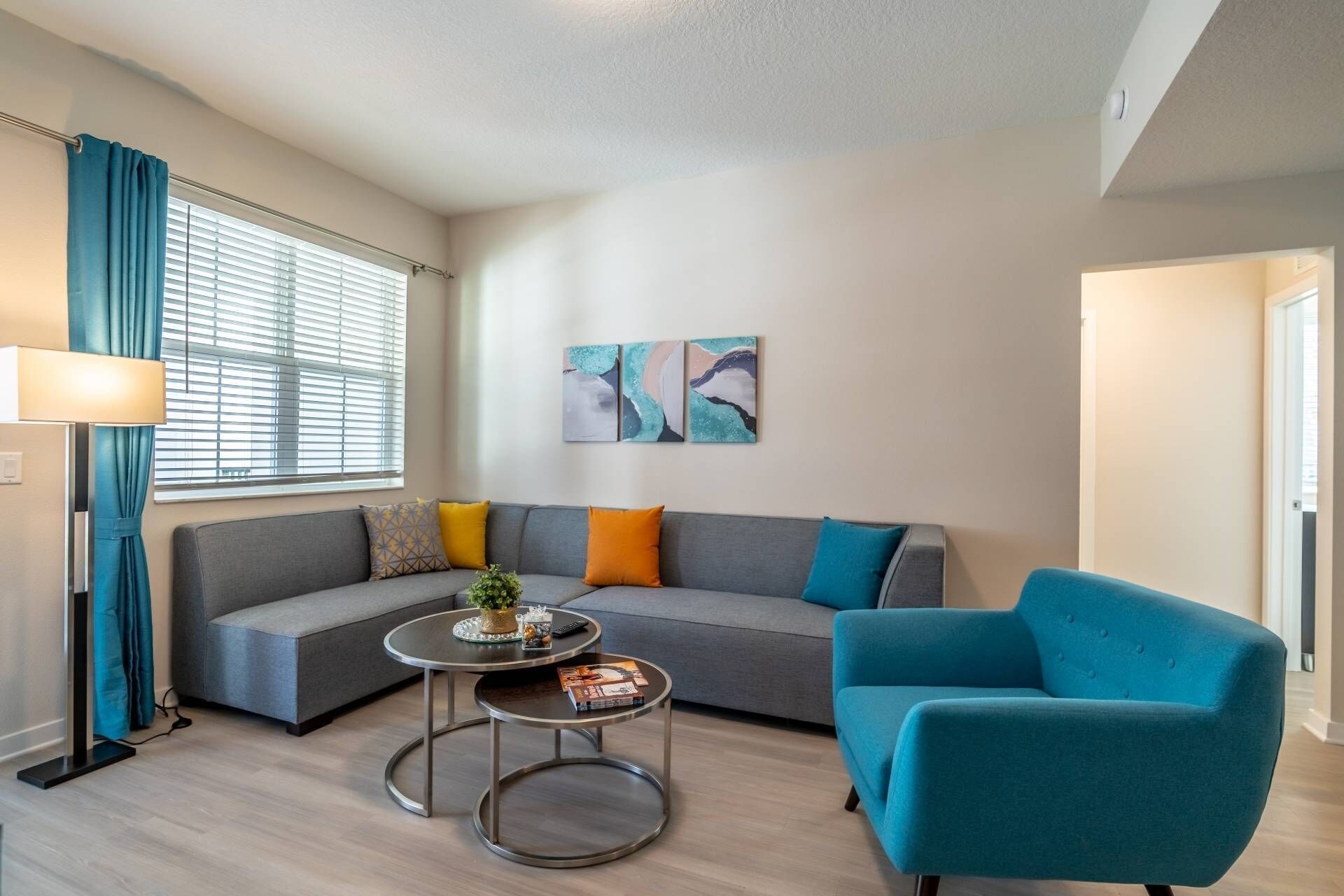 Een moderne woonkamer met een grijze modulaire bank, een ronde salontafel, een blauwe fauteuil en abstracte wanddecoratie.