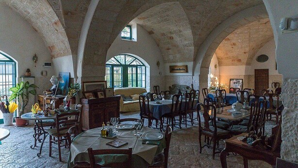 A dining area with multiple tables and chairs, stone arches, and large windows allowing natural light.