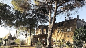 A large, historic building with a prominent tower and arched windows, surrounded by trees and a well-maintained lawn.