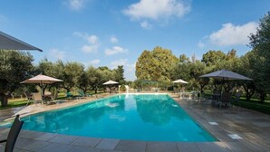 A rectangular swimming pool with clear blue water, surrounded by tiled flooring and shaded by umbrellas.