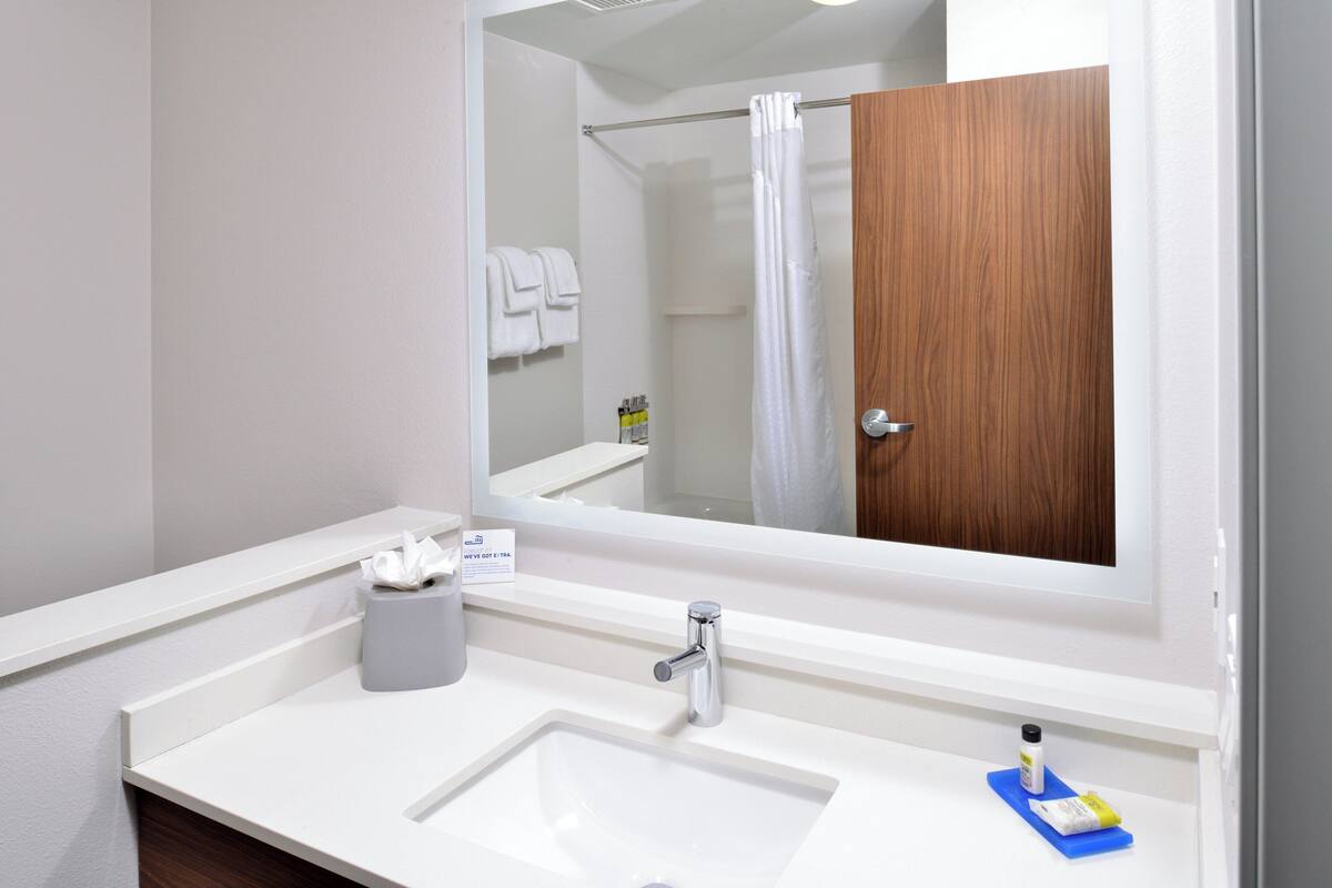 Un baño moderno con un espejo grande, lavamanos blanco y una puerta de madera.