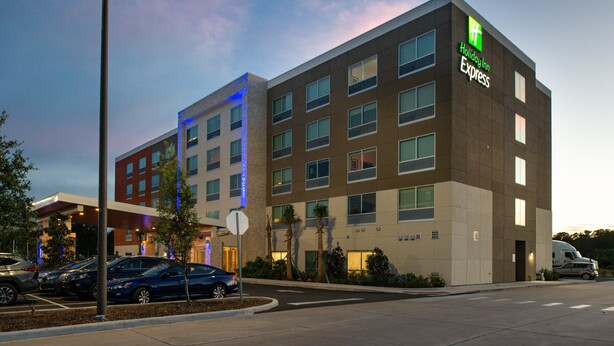 Edificio de Holiday Inn Express con varios pisos, un estacionamiento con varios coches y un farol.