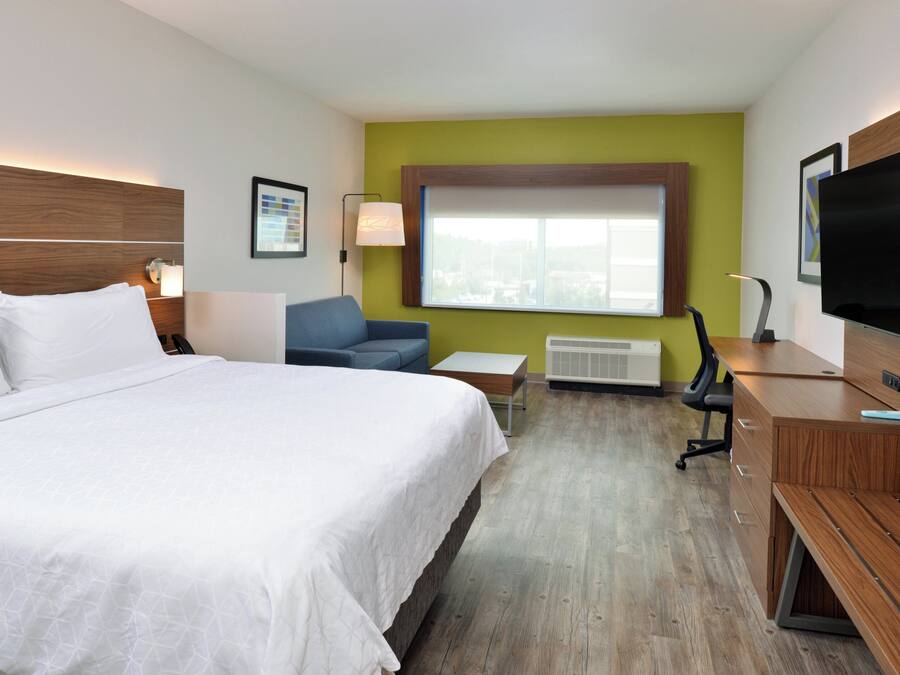 A hotel room with a large bed, a desk, a chair, a television, and a window with a view.