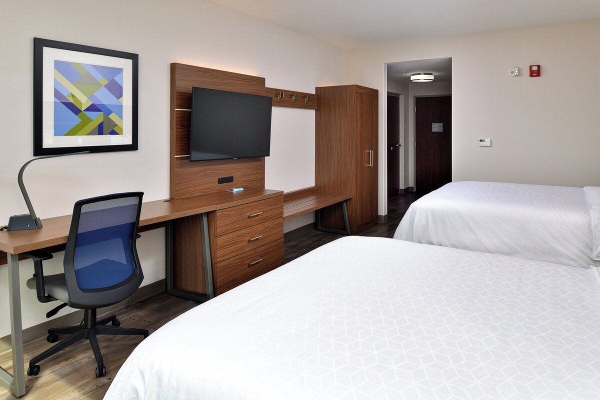 Habitación de hotel con escritorio, silla, televisor, armario y dos camas.