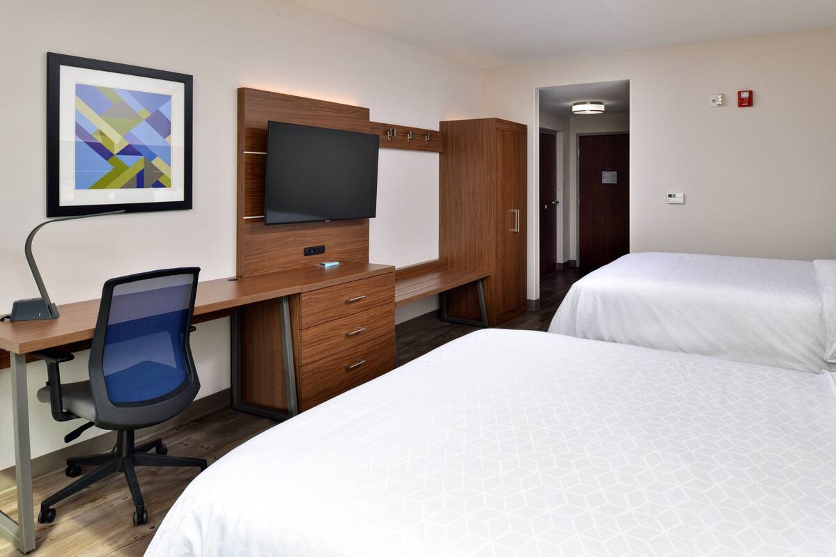 Habitación de hotel con escritorio, silla, televisor, armario y dos camas.