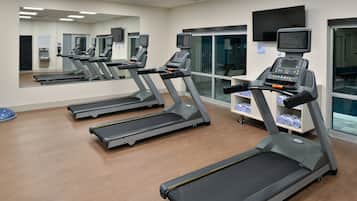 A gym with multiple treadmills, a large mirror, and a television screen.