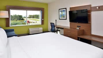 Quarto de hotel com uma cama grande, uma escrivaninha com cadeira, uma televisão e uma janela com vista para áreas verdes e uma estrada.